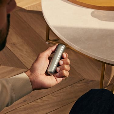 Hand holding Ploom AURA front panel Lunar Silver Augmented Pattern accessory on device.