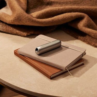 Ploom AURA front panels with Lunar Silver Augmented Pattern placed on top of a stack of notebooks.