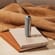 Dispositivo Ploom con Cover Posteriore Lunar Silver in piedi sopra una pila di quaderni