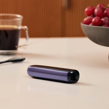 Ploom AURA front panel Lavender device stored on table.