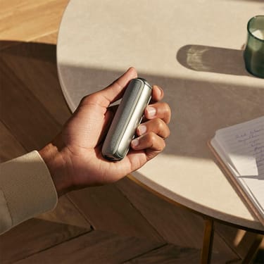 Mano che tiene l'accessorio Cover Posteriore Ploom AURA Lunar Silver sul dispositivo.