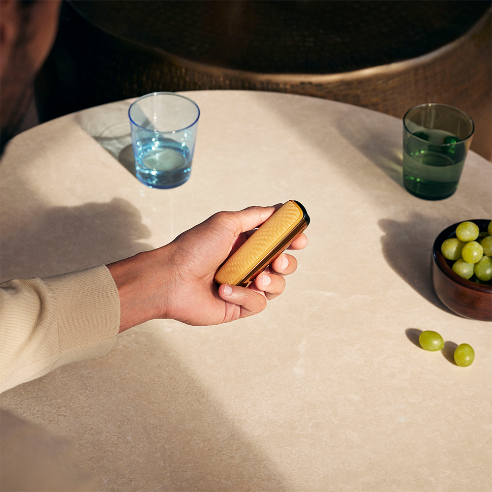 Hand showing Ploom AURA Back Cover Mango Sorbet accessory attached to device.